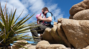 Simon Ohneberg sitzt mit Baby auf einem Stein in der Wüste